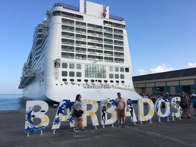 The large white decorative BARBADOS sign at the Bridgetown cruise terminal dock with the Norwegian Epic cruise ship parked directly behind it.