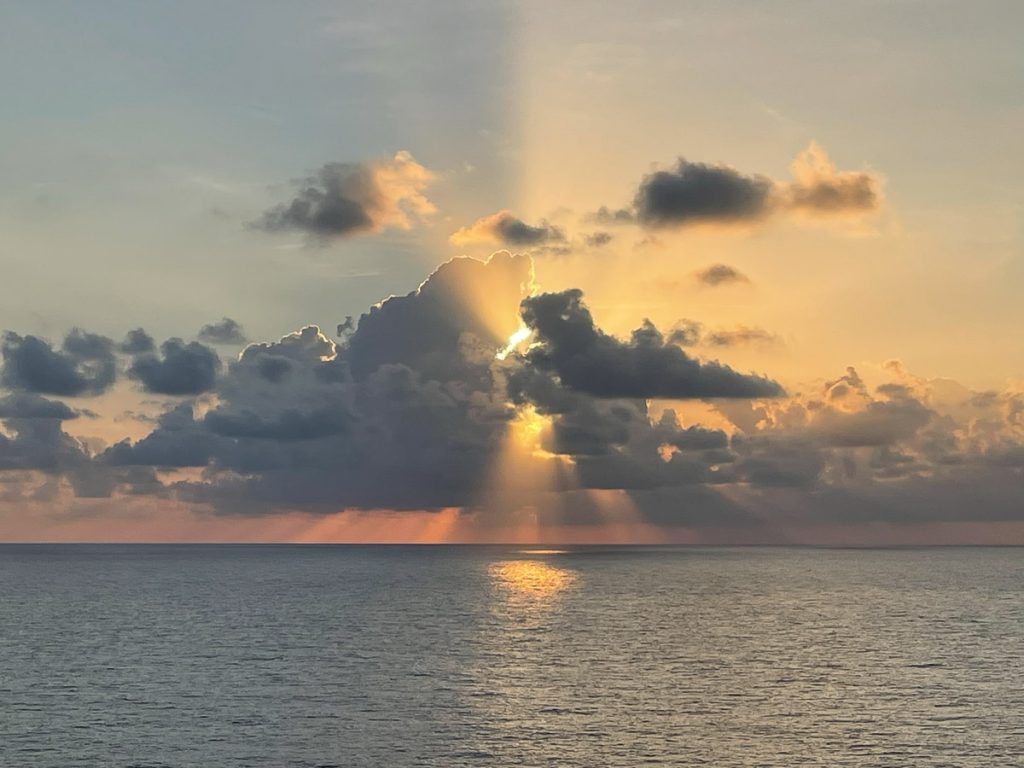 The sun rises over the Gulf of Mexico behind some dark clouds with bright rays shining in between.