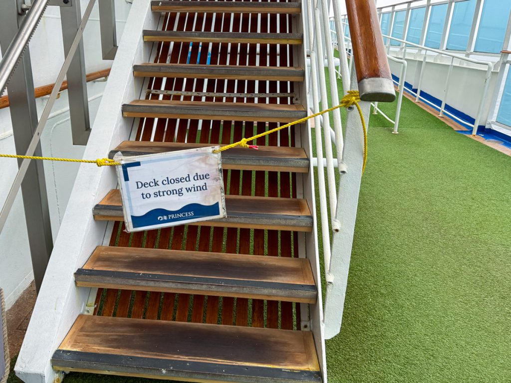 Roped off cruise ship stairs displaying a warning sign that reads Deck closed due to strong wind