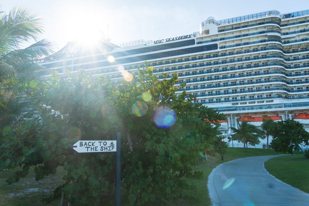Directional sign reading Back to the Ship with the MSC Seashore cruise ship docked in the background on a sunny day