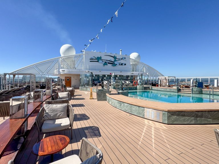 Quiet outdoor Yacht Club pool deck with lounge seating and a swimming pool under a clear blue sky on the MSC Seashore.